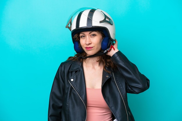 Young caucasian woman with a motorcycle helmet isolated on blue background having doubts