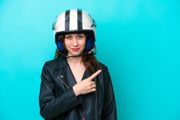 Young caucasian woman with a motorcycle helmet isolated on blue background pointing to the side to present a product