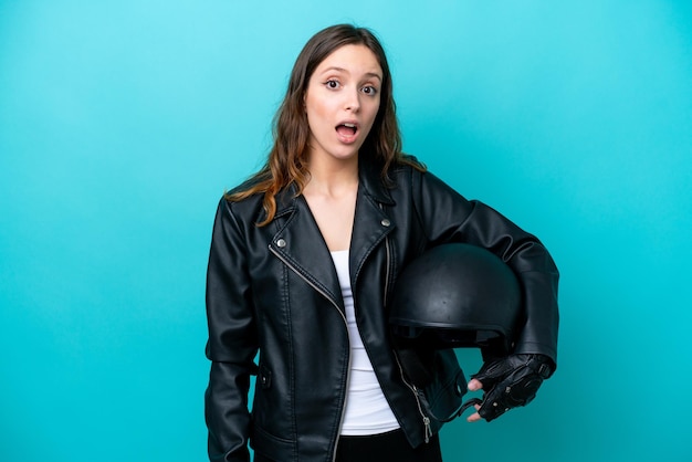 Young caucasian woman with a motorcycle helmet isolated on blue background with surprise facial expression