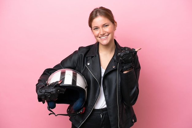 Young caucasian woman with a motorcycle helmet isolated on pink background pointing to the side to present a product