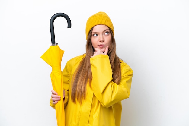 Young caucasian woman with rainproof coat and umbrella isolated on white background and looking up