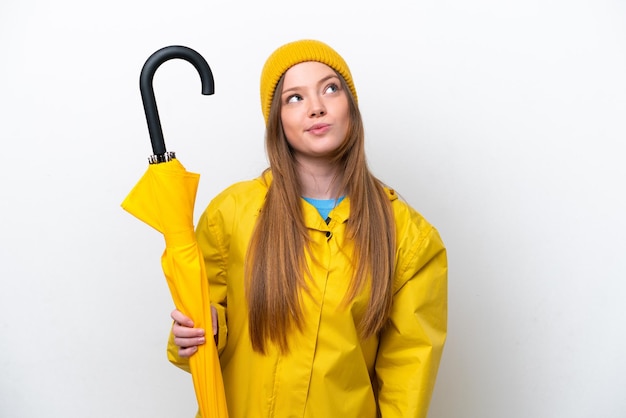 Young caucasian woman with rainproof coat and umbrella isolated on white background and looking up