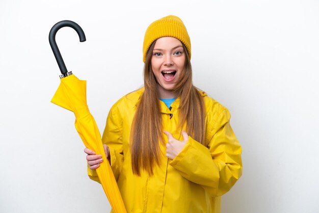 Young caucasian woman with rainproof coat and umbrella isolated on white background with surprise facial expression