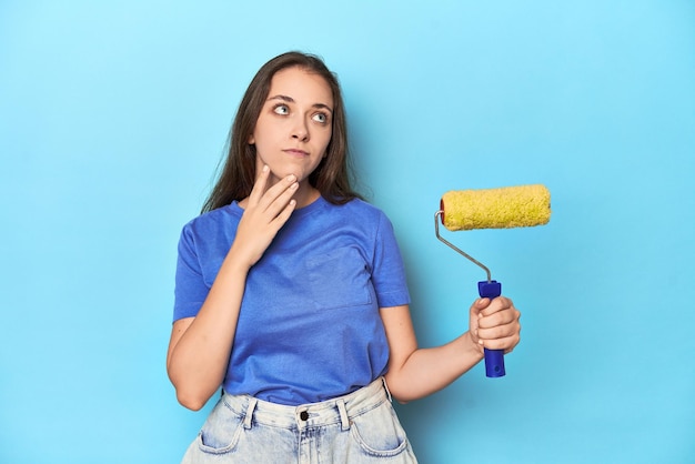 Young Caucasian woman with yellow paint roller on blue studio