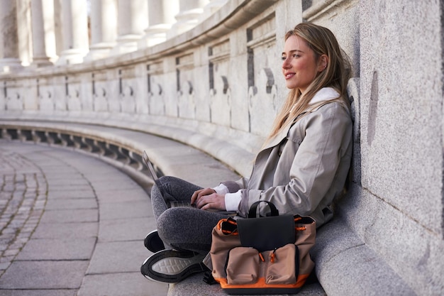 Young Caucasian woman working on laptop outside an old building