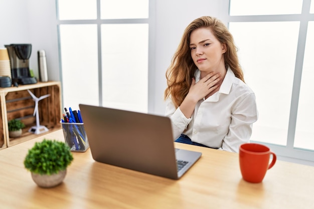 Young caucasian woman working at the office using computer laptop touching painful neck, sore throat for flu, clod and infection