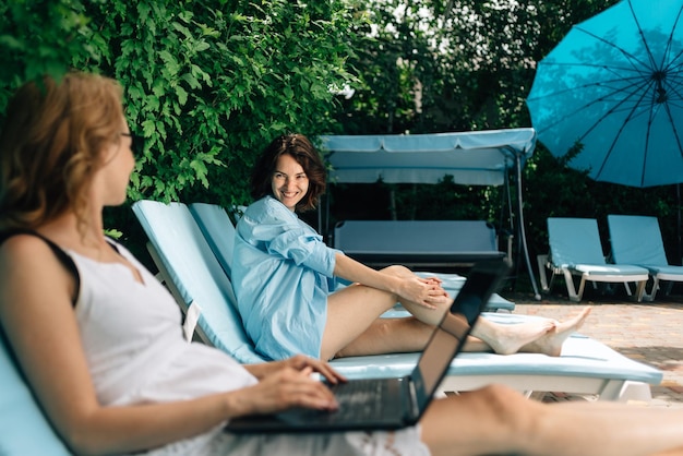 Young caucasian woman working with laptop on vacation Freelance tourist with a girlfriend on a sun lounger Businesswoman using pc at the hotel