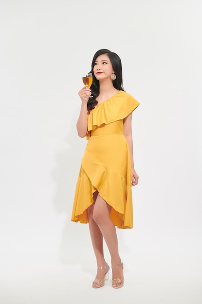 Young celebrating woman yellow dress isolated over studio background hold wine glass