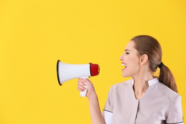 Young chambermaid with megaphone on color wall