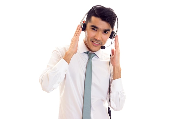 Young charming man with dark hair in white shirt with blue tie using headphones in studio