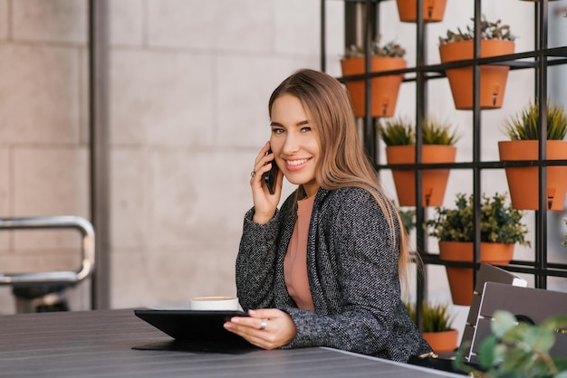 A young charming woman is calling on a mobile phone sitting in a cafe and talking on a mobile phone