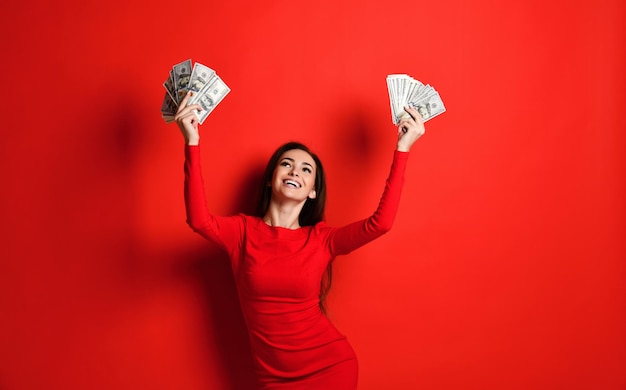 Young cheeky brunette in a red dress rejoices in a large amount of money in her hands she wins