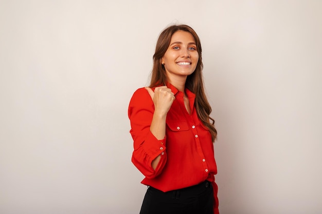 Photo young cheerful blonde woman wearing red shirt is pointing aside with her thumb