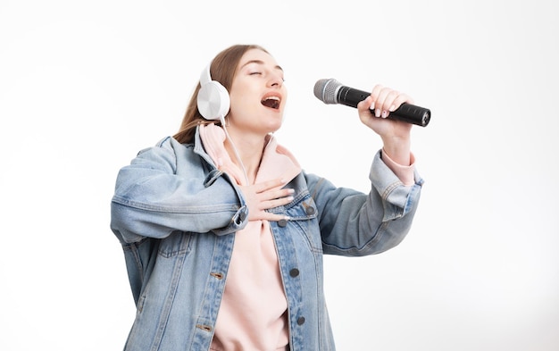 Young cheerful caucasian woman with headphones singing into microphone isolated on white background