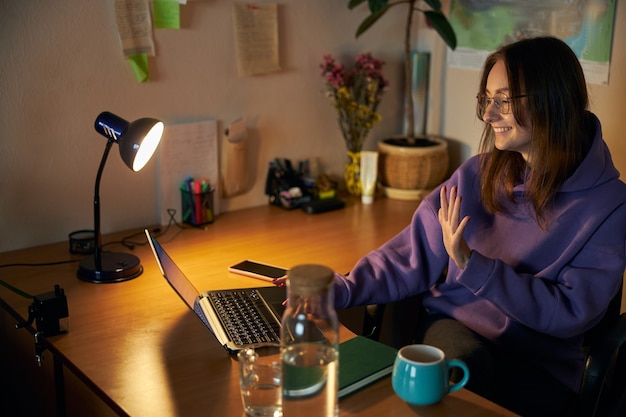 Young cheerful confident and happy freelancer woman is working on laptop at home in the evening