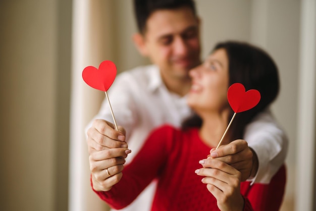 Young cheerful couple in love holding red hearts over eyes and smiling