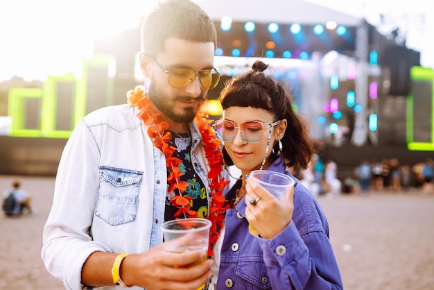 Young and cheerful couple at music festival Happy friends drinking beer and having fun