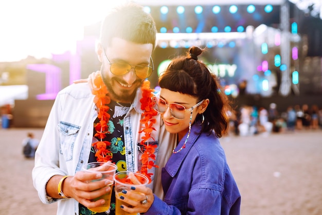 Young and cheerful couple at music festival Happy friends drinking beer and having fun