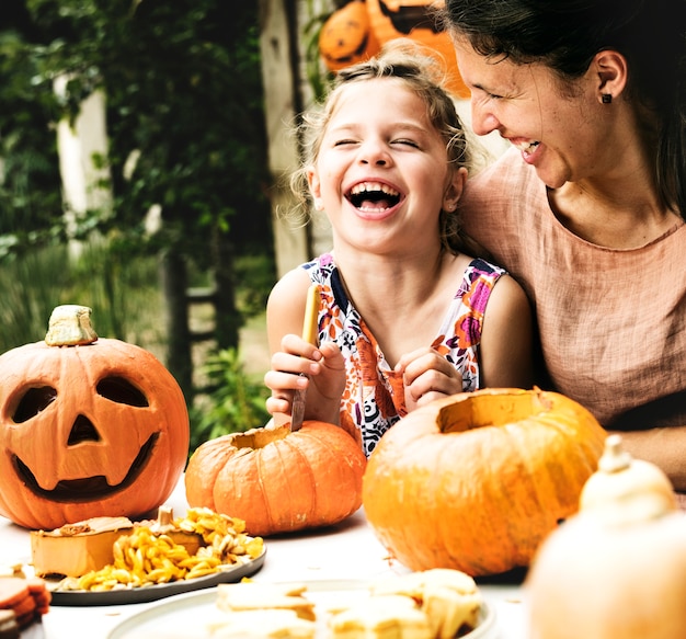 Young cheerful girl carving pumpkins with her mom