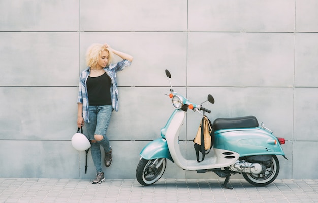 Young cheerful girl driving scooter in in city. Portrait of a young and stylish woman with a moped