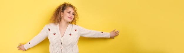 Young cheerful girl smiling at the camera while standing on a yellow background closeup