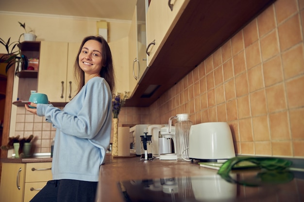 Young cheerful  and happy woman is preparing tasty tea  at her kitchen at home