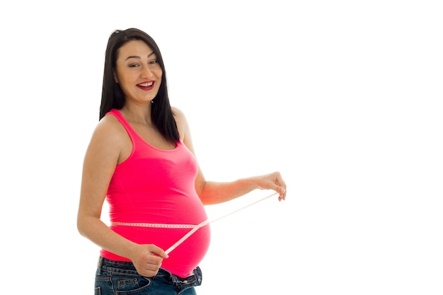 Young cheerful pregnant mother laughing and measure her belly isolated on white background in studio