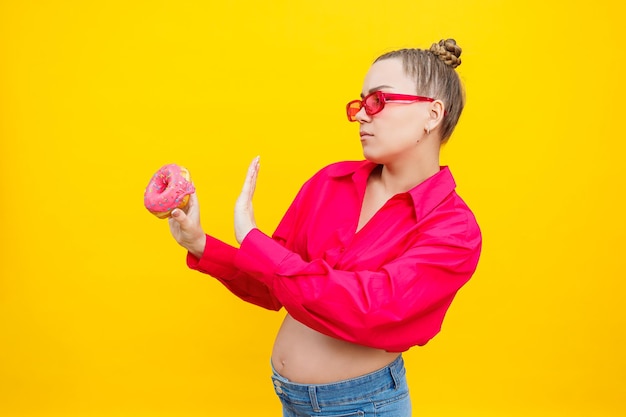 Young cheerful pregnant woman in pink shirt isolated on yellow background holding donuts with a cheerful expression on her face Sweet food during pregnancy