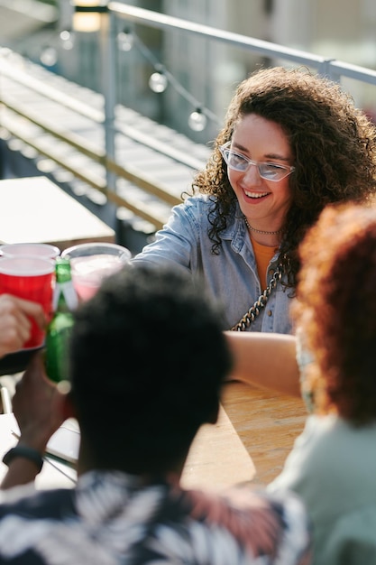 Young cheerful woman in eyeglasses and casualwear toasting with her friends