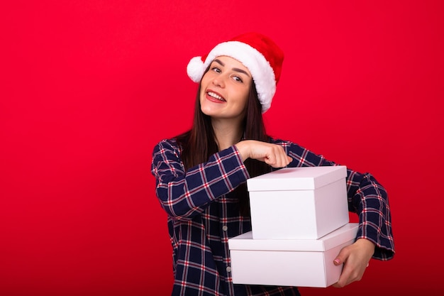 A young cheerful woman in festive pyjamas holds New Year's gifts on a red background in the studio