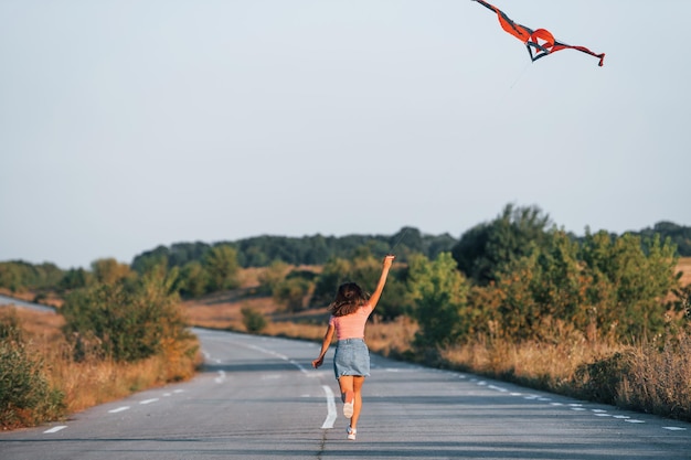 Young cheerful woman having fun with kite outdoors on the road