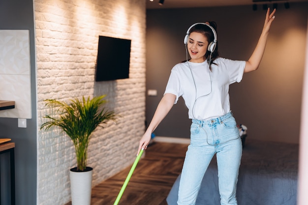 Young cheerful woman is washing floor in room with mop having fun