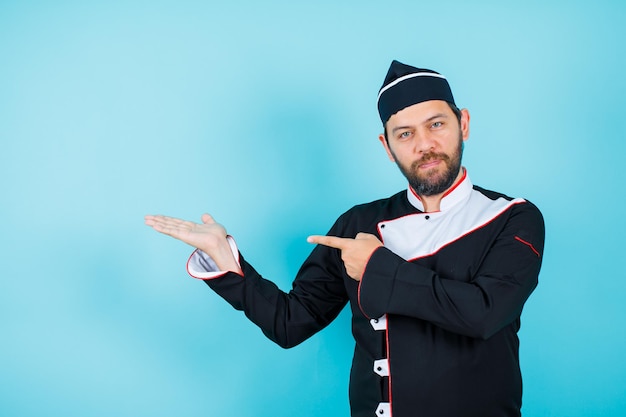 Young chef is raising up his handful and showing it with forefinger on blue background