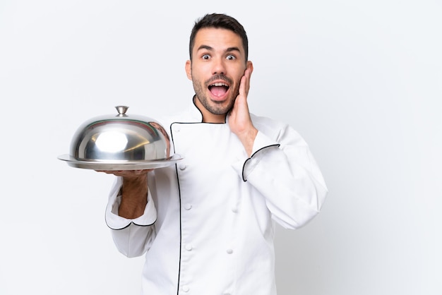 Young chef with tray isolated on white background with surprise and shocked facial expression