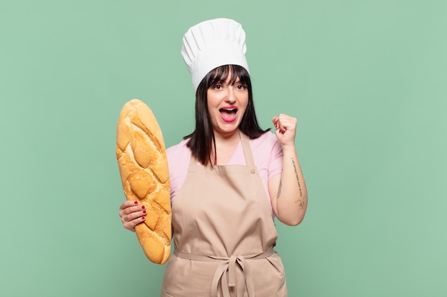 Young chef woman feeling shocked, excited and happy, laughing and celebrating success, saying wow!