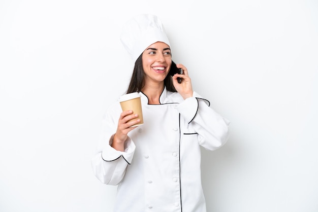 Young chef woman over white background holding coffee to take away and a mobile