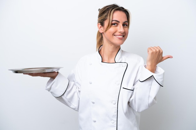 Young chef woman with tray isolated on white background pointing to the side to present a product