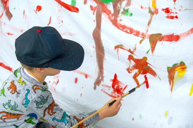 Photo young child creating a colourful abstract painting with a paintbrush on a sheet