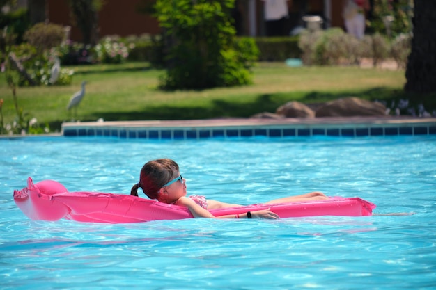 Young child girl relaxing on summer sun swimming on inflatable air mattress in swimming pool during tropical vacations Summertime activities concept