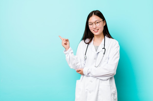 Young chinese doctor woman smiling cheerfully pointing with forefinger away.