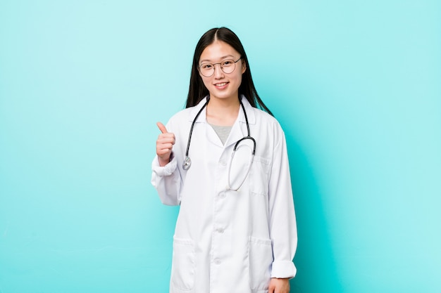 Young chinese doctor woman smiling and raising thumb up