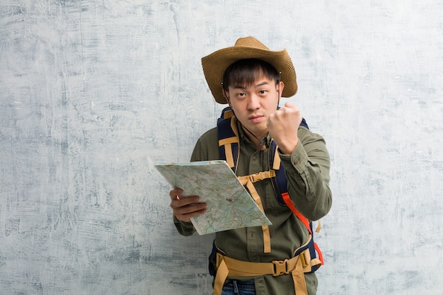 Photo young chinese explorer man holding a map showing fist to front, angry expression