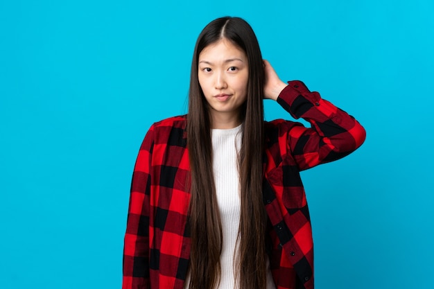 Young Chinese girl over isolated blue background having doubts