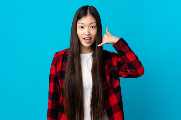 Young Chinese girl over isolated blue background making phone gesture. Call me back sign