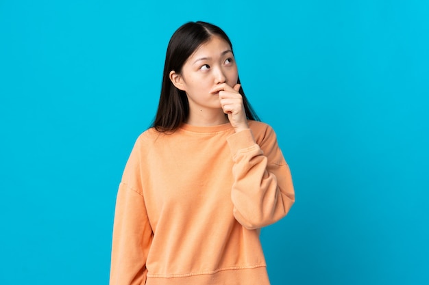 Young Chinese girl on isolated blue having doubts and with confuse face expression