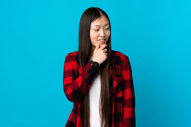 Young Chinese girl on isolated blue looking to the side and smiling