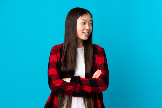 Young Chinese girl on isolated blue with arms crossed and happy