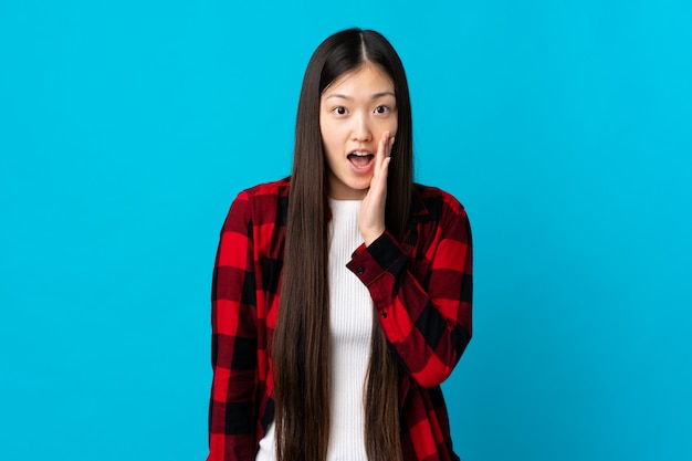 Young Chinese girl on isolated blue with surprise and shocked facial expression