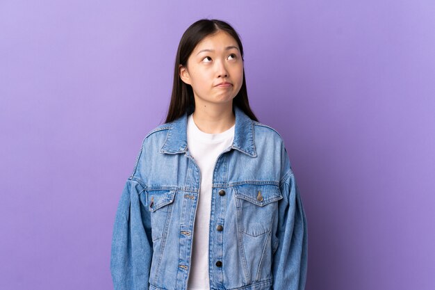 Young Chinese girl over isolated purple and looking up