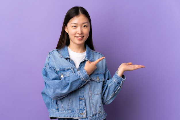 Young Chinese girl over isolated purple wall holding copyspace imaginary on the palm to insert an ad